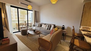 Ein modernes Wohnzimmer mit einer Couch, einem Couchtisch und Korbstühlen. Es gibt einen Essbereich mit Tisch und Stühlen. Das Zimmer hat große Fenster und einen Blick ins Freie.