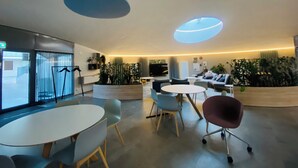 Een moderne wachtruimte met een ronde tafel, stoelen, banken en potplanten.