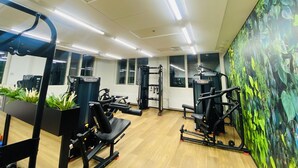 Een sportschool met diverse fitnessapparaten, grote ramen en een muurschildering.