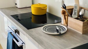 Een moderne keuken met een zwart inductiekookplaatje, een gele pan, een broodrooster en een houten messenblok met een lepel en mes.
