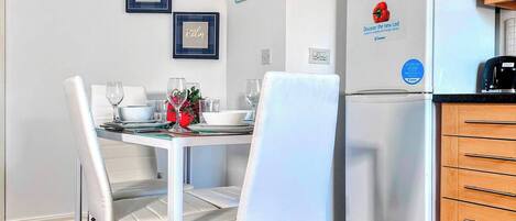 A compact kitchen with a refrigerator, a dining table with chairs, and wall decorations.