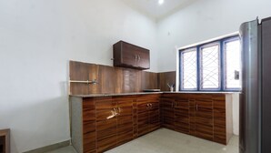 A kitchen with wooden cabinets, a window with bars, and a refrigerator. - Serene 2-bedroom with AC and Kitchen in vibrant Dehradun (Dehradun)