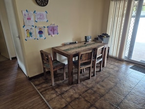 A wooden dining table with chairs, a clock on the wall, and children's drawings taped to the wall.