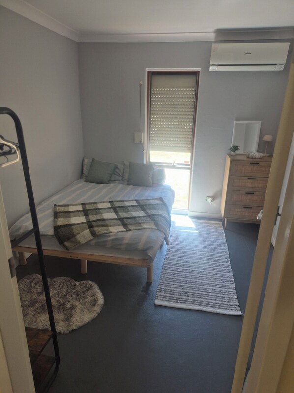 A bedroom with a bed, a dresser, a radiator, and a window with blinds.