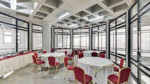 A spacious room with large windows, round tables with red chairs, and a tiled floor. - Ayatti By Caparo (Greater Noida)