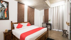 A bedroom with a wooden bed, red and white bedding, a small bedside table, a desk, and a chair. - Ayatti By Caparo (Greater Noida)