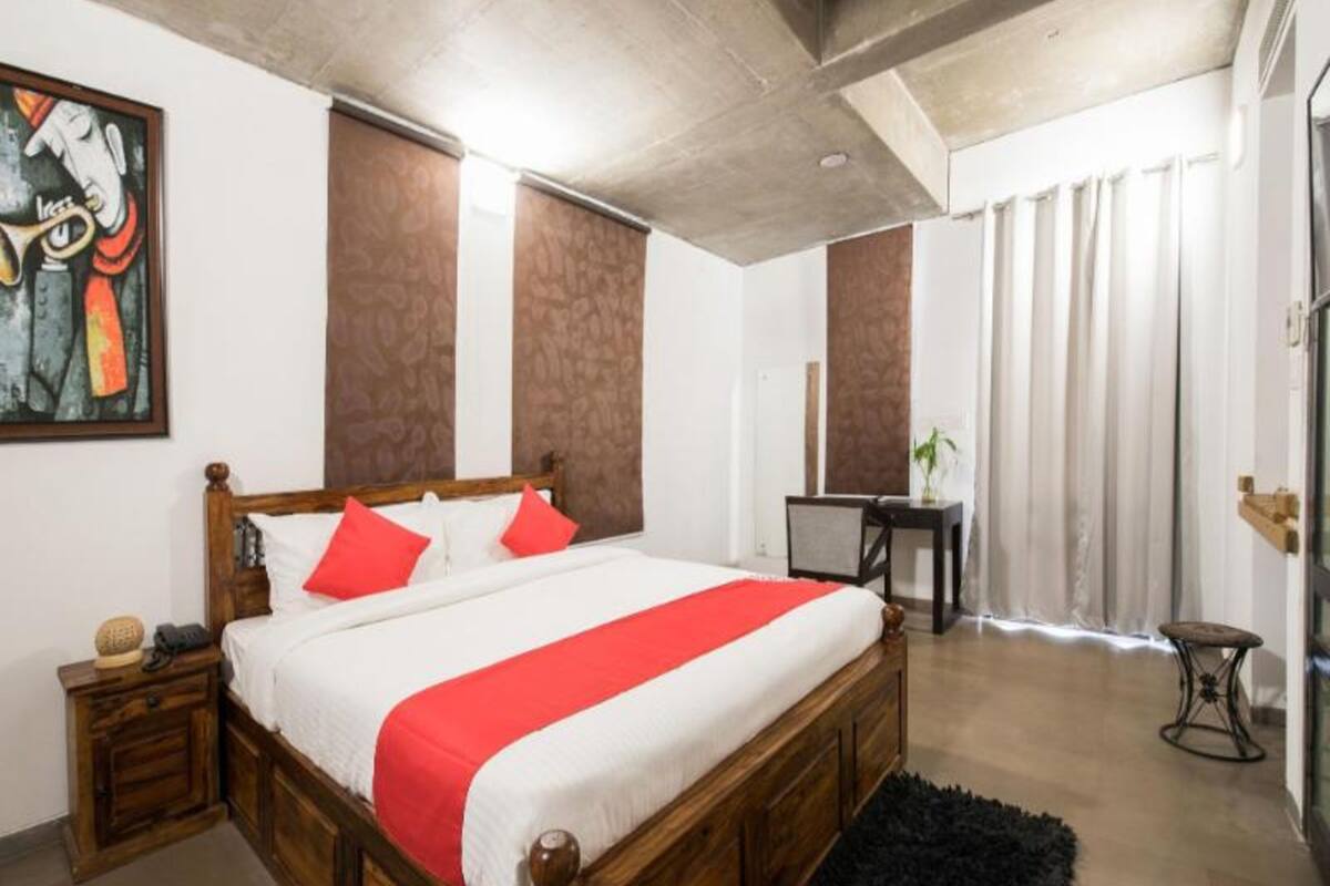 Un dormitorio con una cama de madera, ropa de cama roja y blanca, una mesita de noche pequeña, un escritorio y una silla.