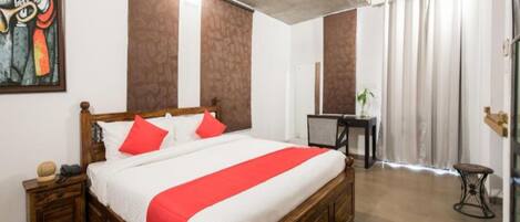 A bedroom with a wooden bed, red and white bedding, a small bedside table, a desk, and a chair.