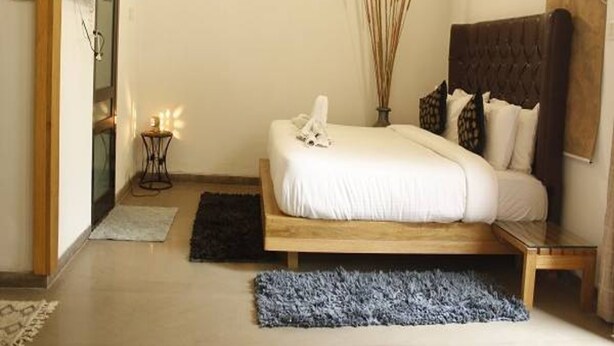 A bedroom with a bed, bedside tables, a wall-mounted TV, and a decorative vase. - Ayatti By Caparo (Greater Noida)