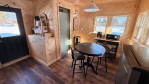 Une cuisine de taille réduite avec des murs en bois, une table à manger, des chaises, un réfrigérateur, un four à micro-ondes et une fenêtre donnant sur l’extérieur.