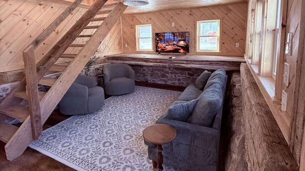 Une pièce mansardée chaleureuse avec un plafond en bois, une grande fenêtre, une télévision et un canapé.