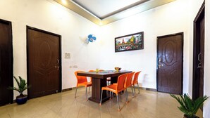 Une salle de conférence avec une table en bois et des chaises orange, deux plantes en pot et un tableau représentant un paysage urbain accroché au mur.