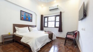 Une chambre avec un grand lit, une table de chevet avec une lampe, une fenêtre avec des rideaux et un téléviseur fixé au mur.