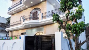Une maison moderne à deux étages, dotée d’un balcon incurvé, d’une entrée sécurisée par un portail et d’un arbre dans le jardin avant.