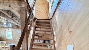 Un escalier intérieur en bois avec une rampe, des murs en bois et une fenêtre visible.