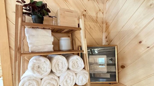 Une étagère en bois avec des serviettes, une plante en pot et un tableau encadré, dans une pièce aux murs en bois et aux plafonds inclinés.