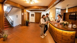 A reception area with a wooden reception desk, a staircase, and a potted plant. - Ferienhof Alte Post (Gitschtal)