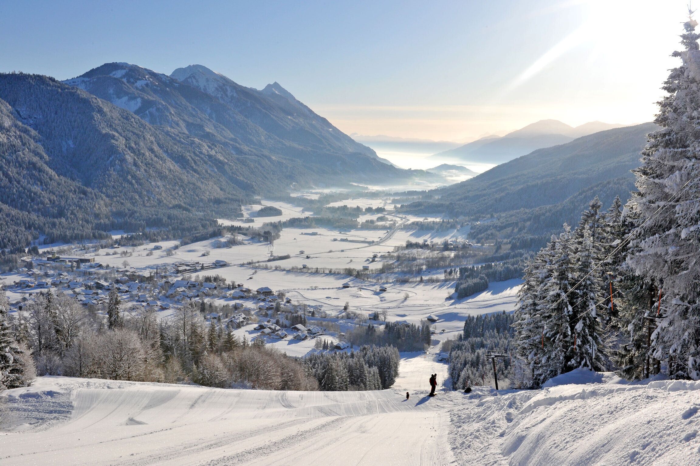 Een besneeuwd berglandschap met een wintersportgebied, inclusief skipistes en een stad in de vallei.