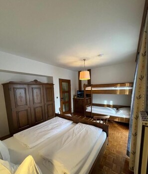 A hotel room with a single bed, a bunk bed, wooden wardrobe, and a desk with a lamp. - Ferienhof Alte Post (Gitschtal)