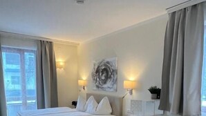 A modern hotel room with a large bed, a desk, and a chair. There are two wall-mounted lamps and a large abstract painting on the wall. - Ferienhof Alte Post (Gitschtal)