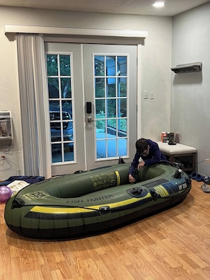 A room with a large inflatable raft, a door with glass panels, and a small table with a plant. - Welcome to our 3 bedroom, 2 bathroom Beaver Lake cabin, where lake views and quiet woods set the scene for an easy escape.<br>• Spacious deck with lake views and outdoor dining<br>• About 2 minutes from Beaver Lake's public boat ramp and hiking/bikin (Rogers)