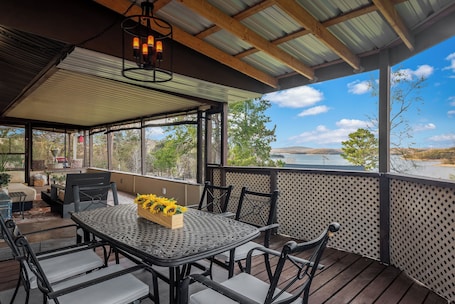 A covered outdoor patio with a table and chairs, a wooden deck, and a view of the landscape.