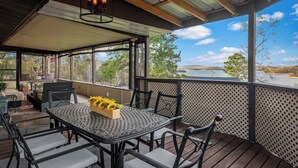 An outdoor patio with a table and chairs, a hanging light fixture, and a view of a lake and hills.