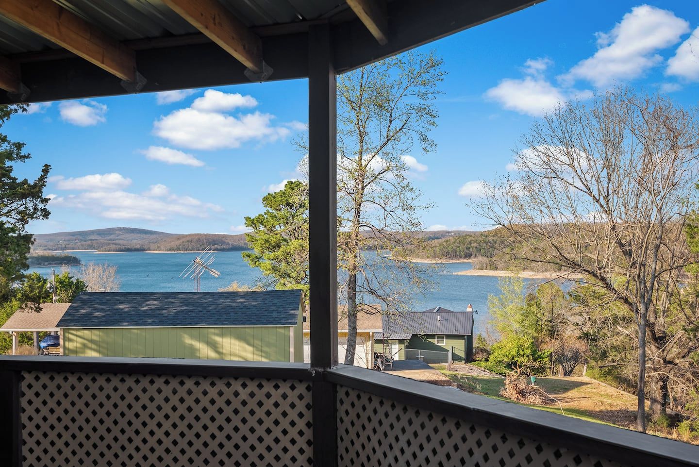 Une vue depuis un porche abrité donnant sur un lac, avec des bâtiments et des arbres au premier plan.