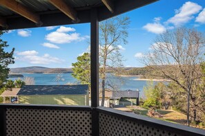 Blick von einer überdachten Veranda auf einen See, im Vordergrund befinden sich Gebäude und Bäume.