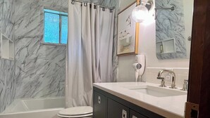 A bathroom with a bathtub, toilet, vanity with a mirror, and a window with curtains.