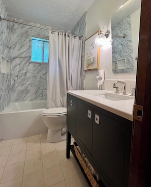 A bathroom with a bathtub, toilet, vanity with a mirror, and a window with curtains.