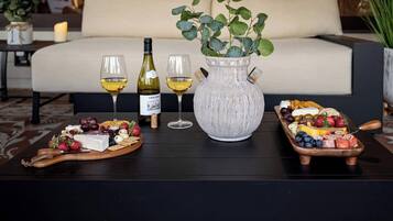 A dining table with a wine bottle, glasses, a vase with green leaves, and a fruit and cheese board.