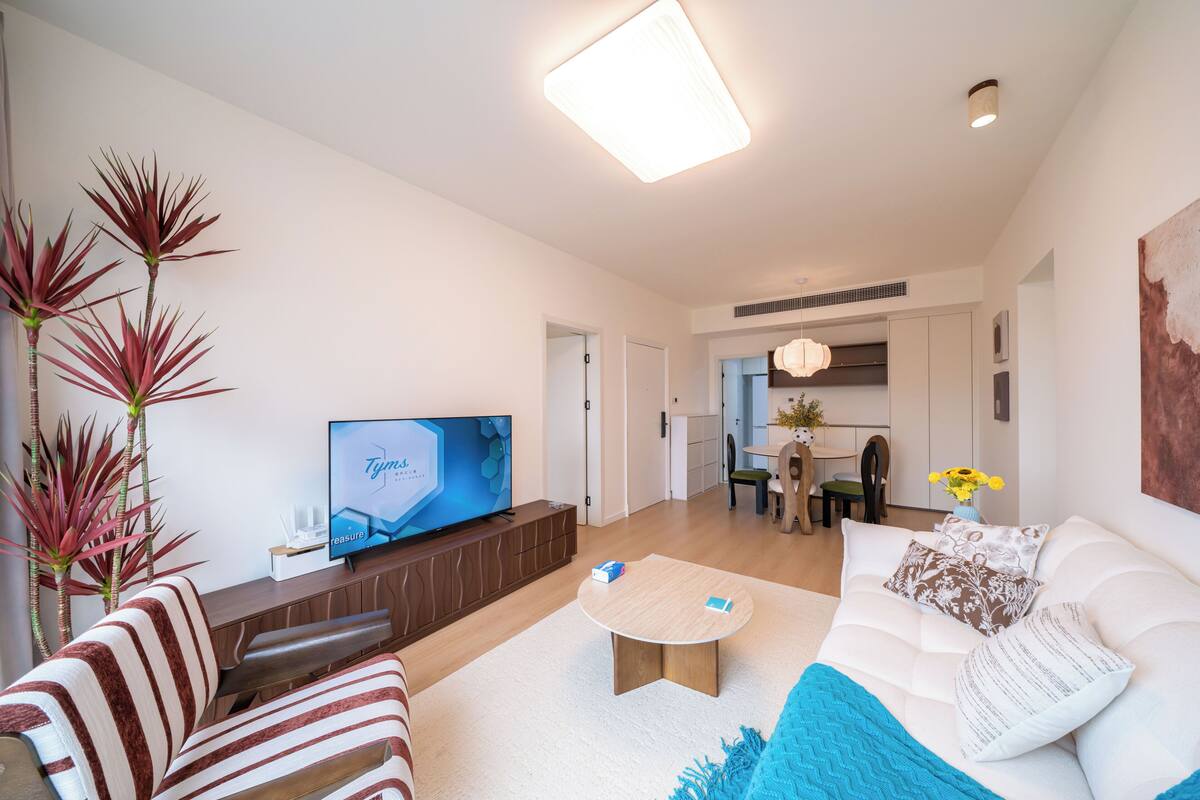 Una sala de estar moderna con una televisión de pantalla plana, un sofá, una mesa de centro y un comedor al fondo.