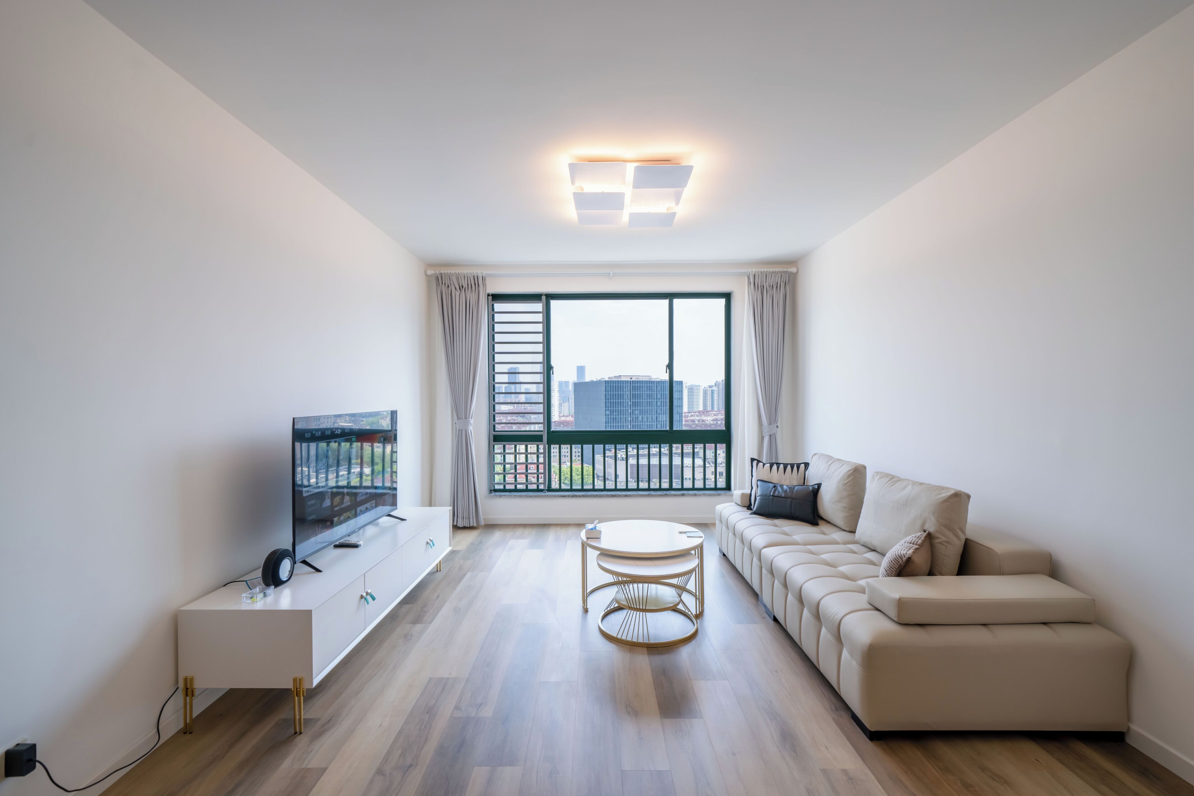 Uma sala de estar moderna com uma televisão de tela plana, um sofá, uma mesa de centro e uma grande janela com vista para a cidade.