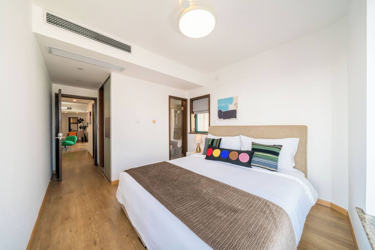 Una habitación de hotel con una cama, cabecero, una obra de arte en la pared y suelo de madera.