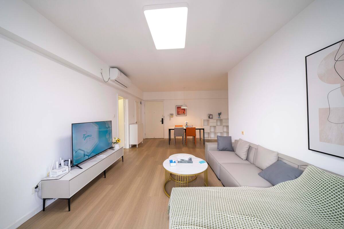 Una sala de estar moderna con televisor de pantalla plana, un sofá, una mesa de centro y un comedor al fondo.