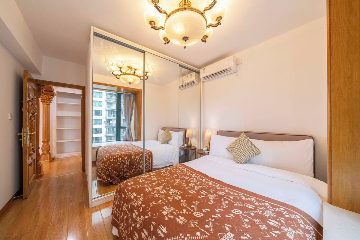 Habitación de hotel con un espejo grande, una cama con colcha estampada, una mesita de noche con lámparas y un candelabro en el techo.