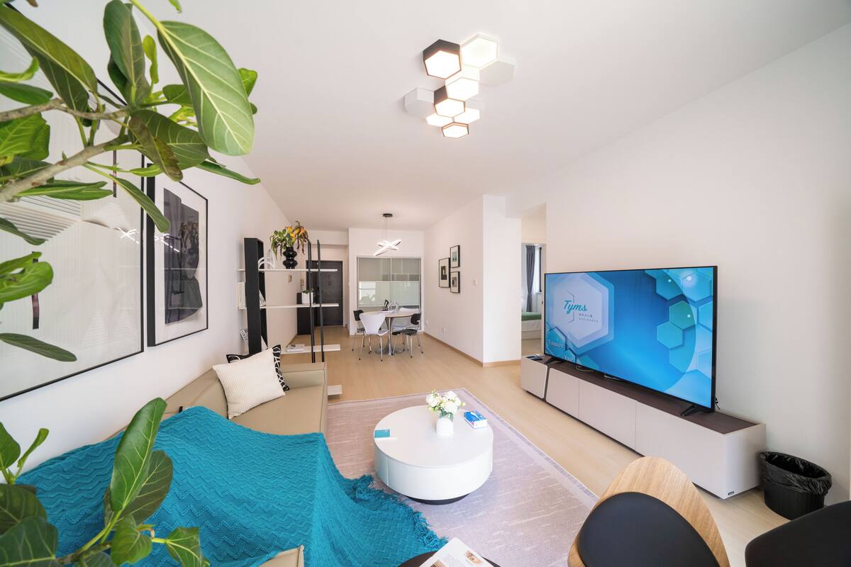 Una sala de estar moderna con una televisión de pantalla plana, una mesa de centro redonda y un comedor al fondo.