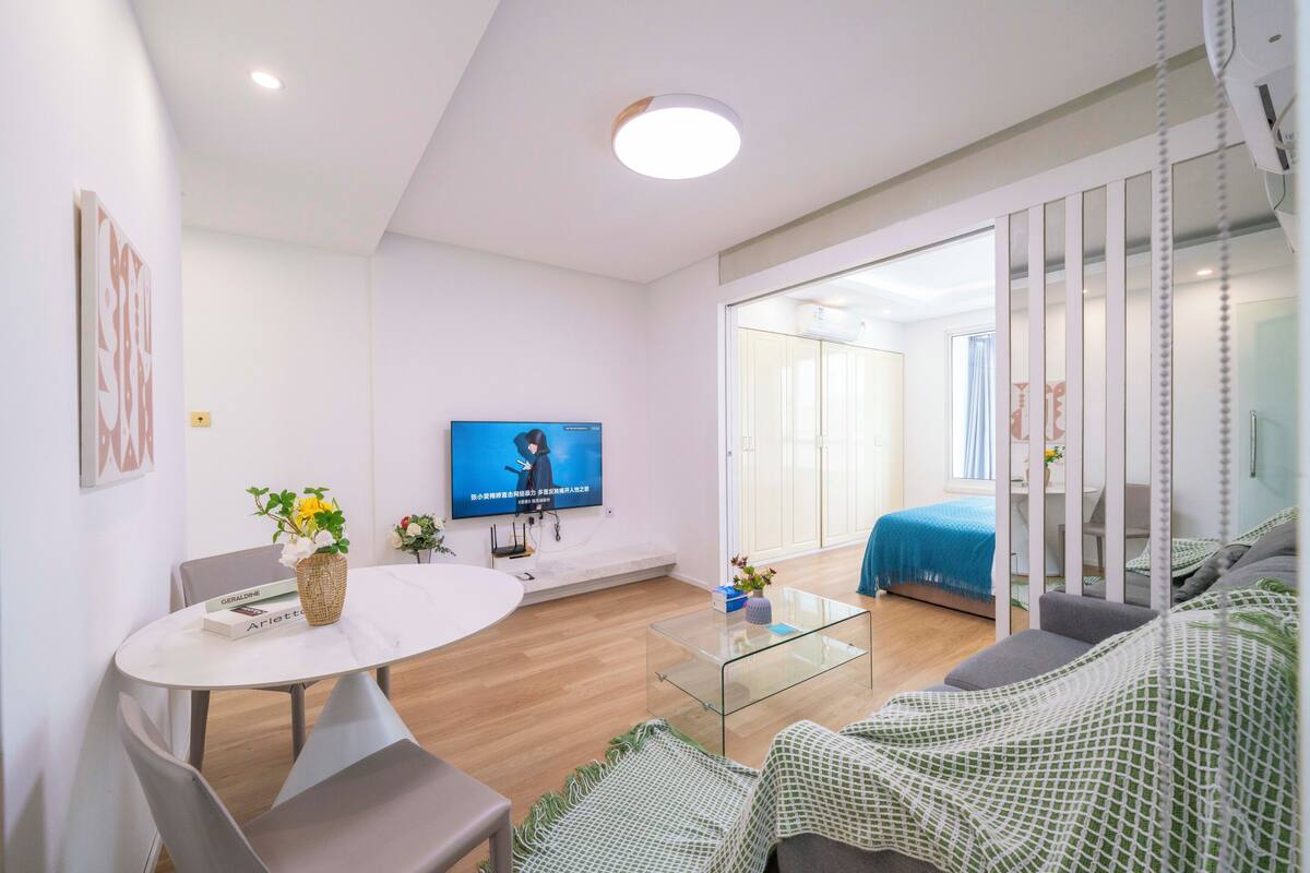 Una sala moderna con una mesa de centro de vidrio, un sofá, un televisor y un comedor con sillas y una mesa pequeña.