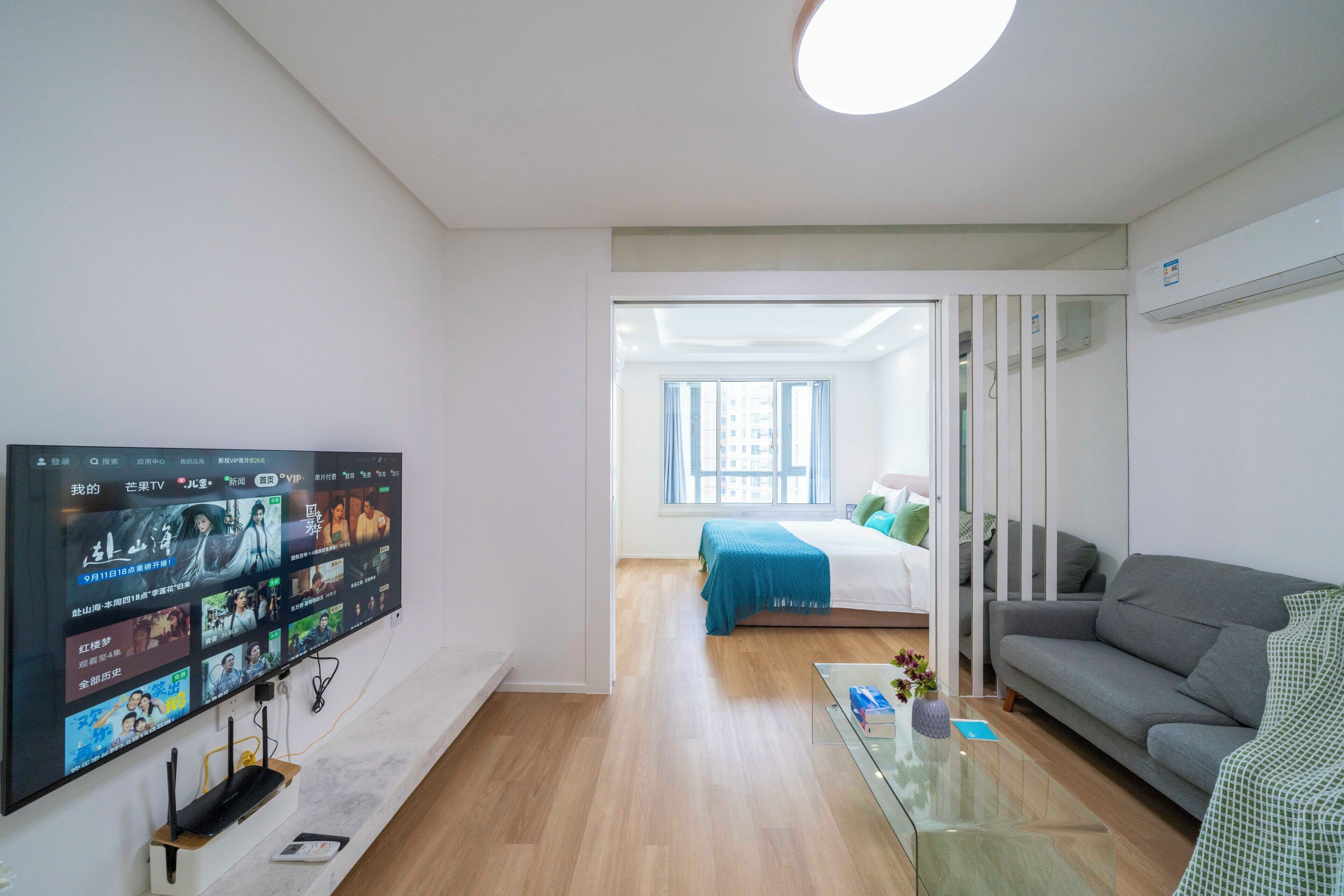 Un saló modern amb televisió de pantalla plana, un sofà, una taula de centre de vidre i un llit amb edredó blau.