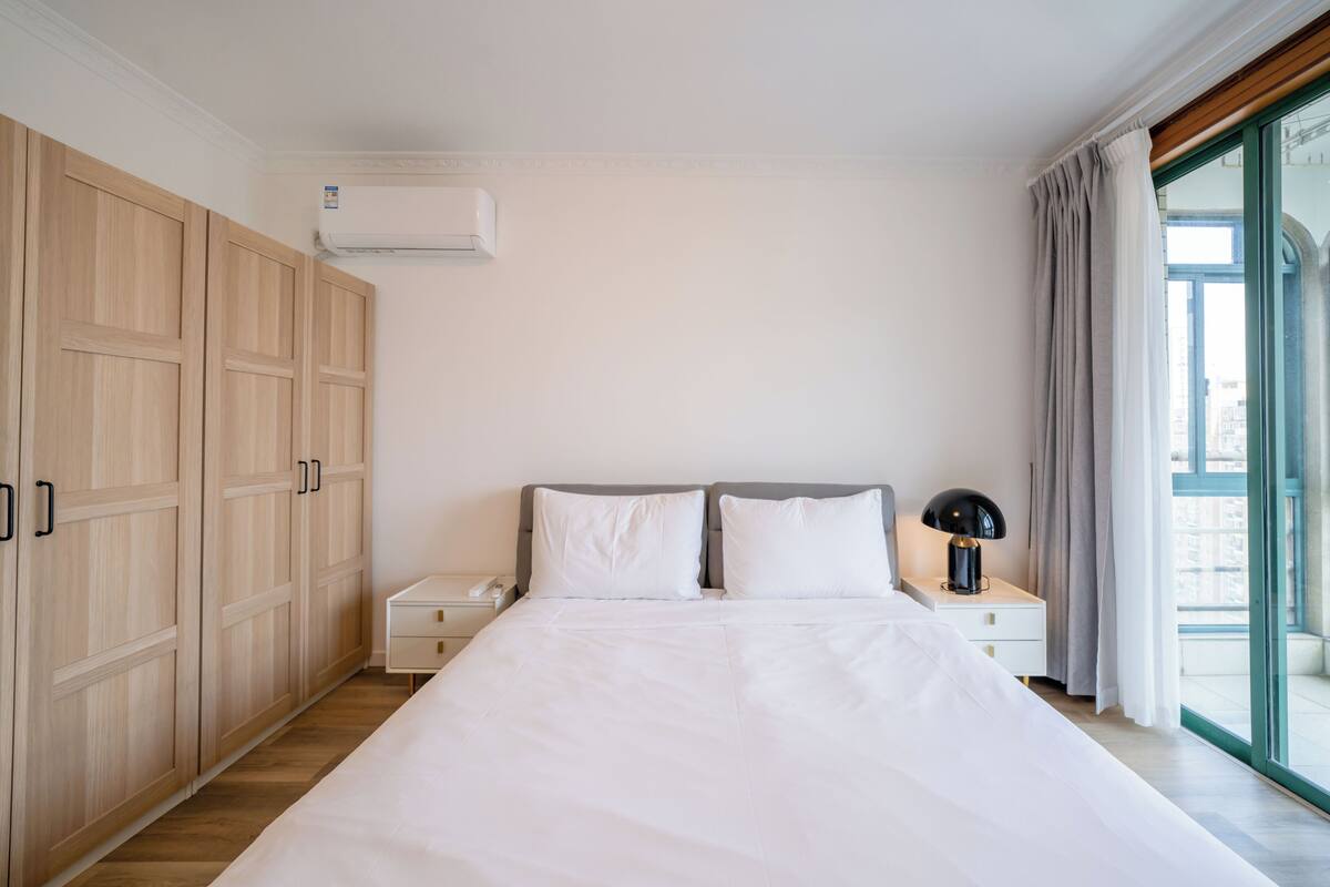 Un dormitorio con una cama grande, armario de madera, mesita de noche y ventana con cortinas.