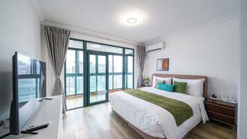 A hotel room with a bed, a TV, a desk, and a view of the city through large windows.