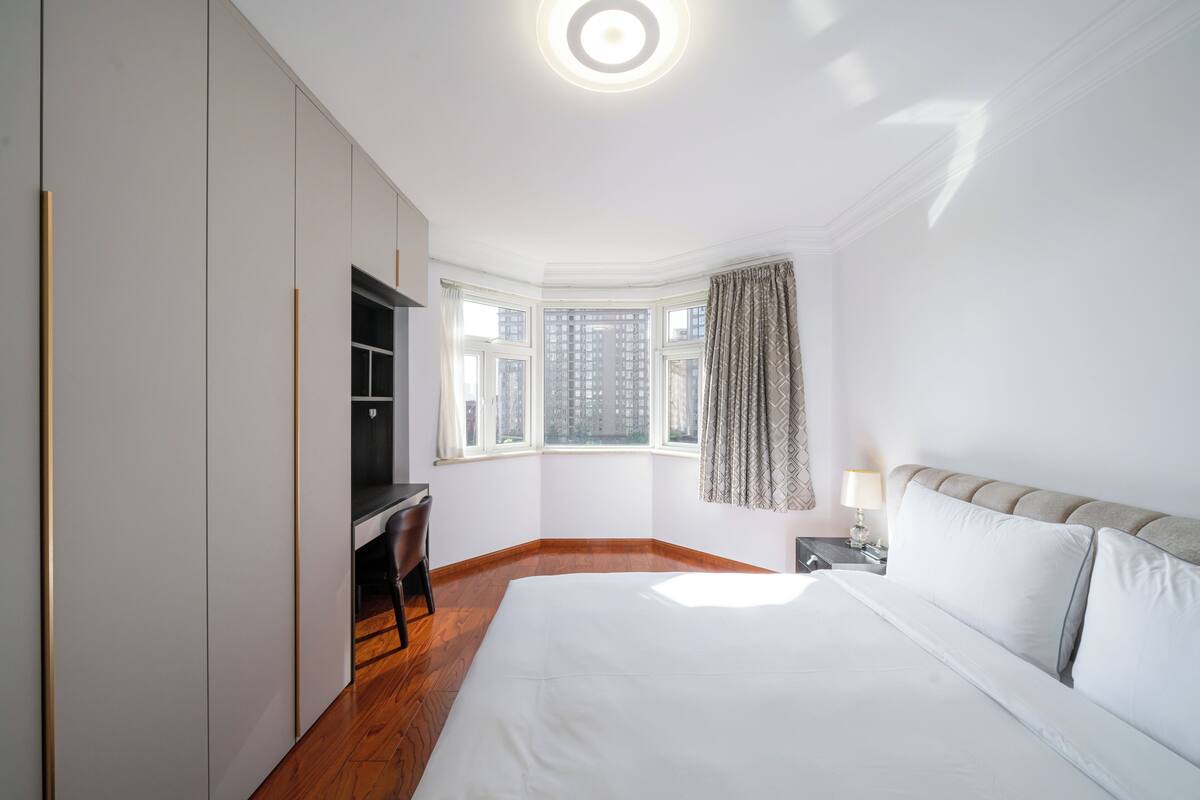 Un dormitorio con una cama grande, un escritorio y una ventana con cortinas.