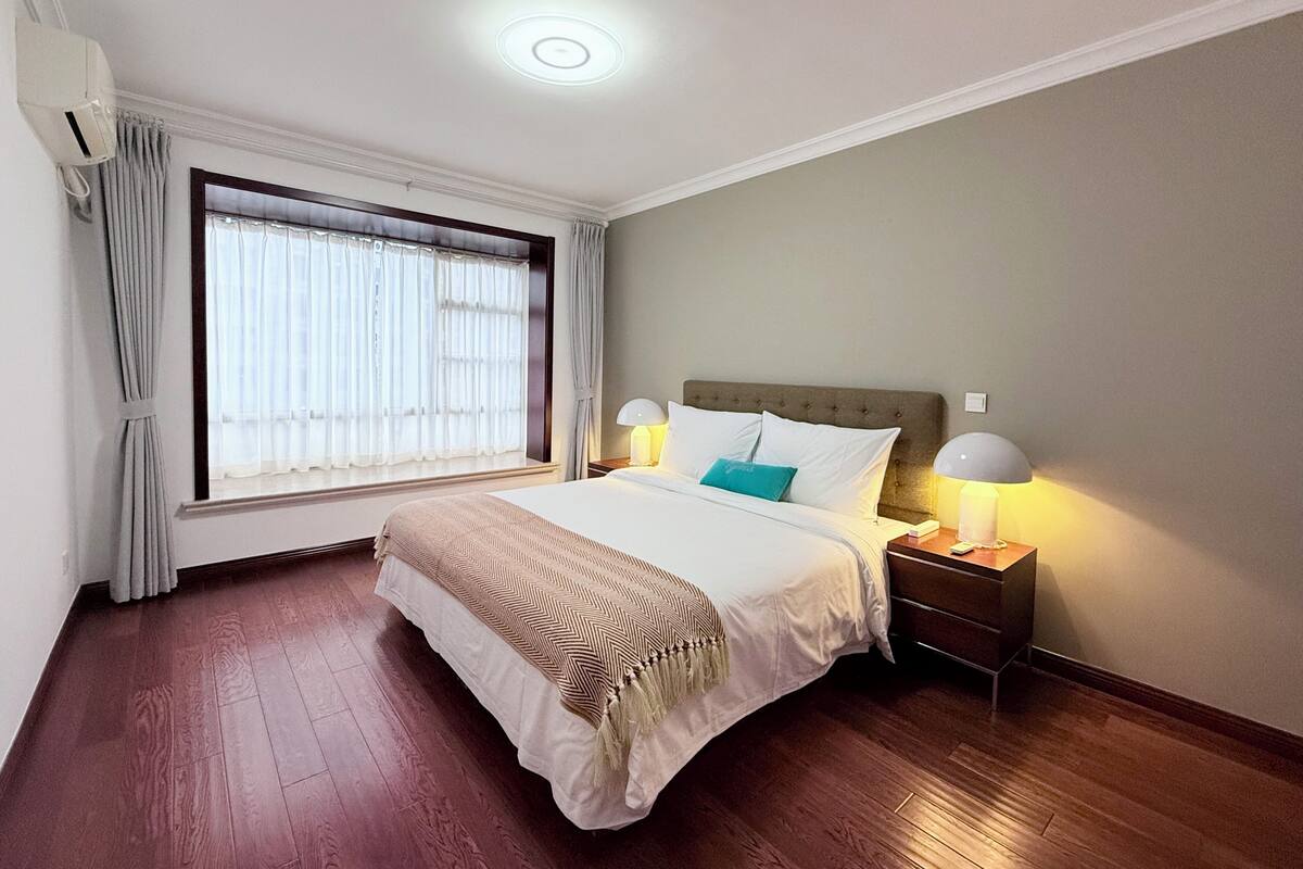 Una habitación de hotel con una cama grande, dos lámparas de noche, una ventana con cortinas y una luz en el techo.