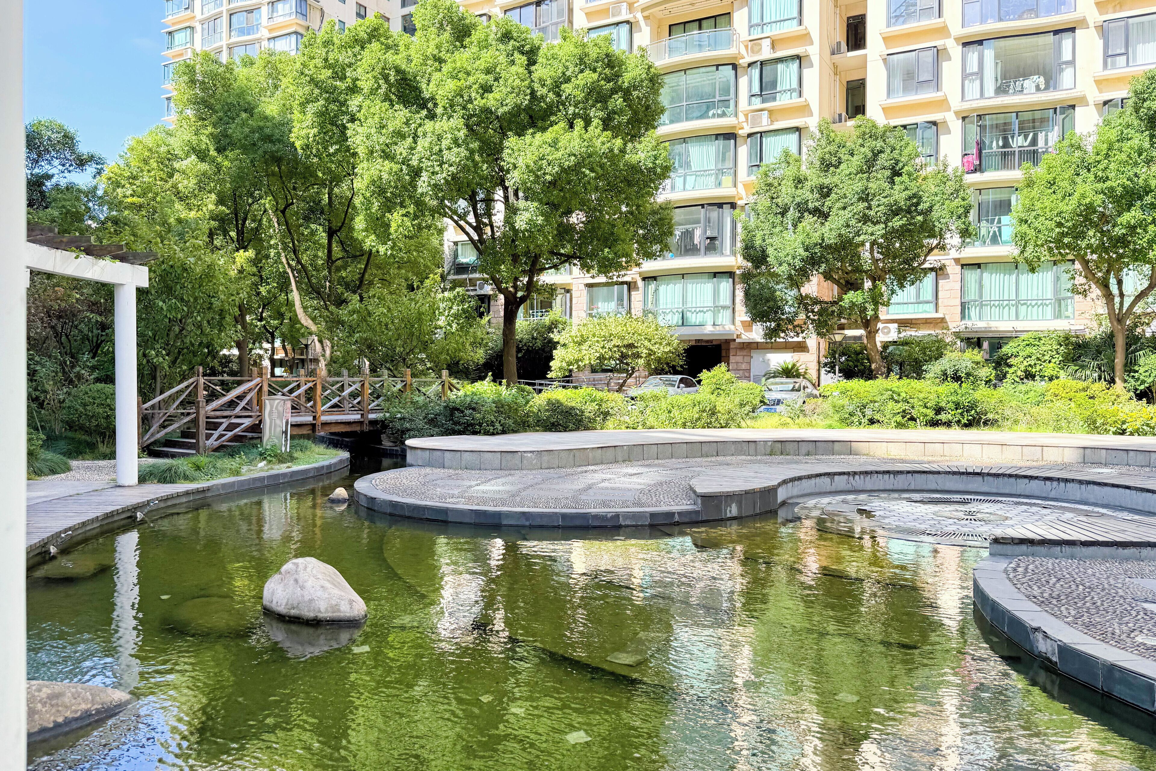 Un immeuble résidentiel doté de nombreux balcons, d’un petit pont et d’un élément décoratif aquatique de forme circulaire.
