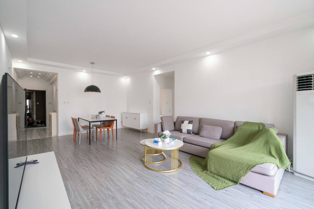 Una sala de estar moderna con comedor, un sofá con una manta verde y un televisor.