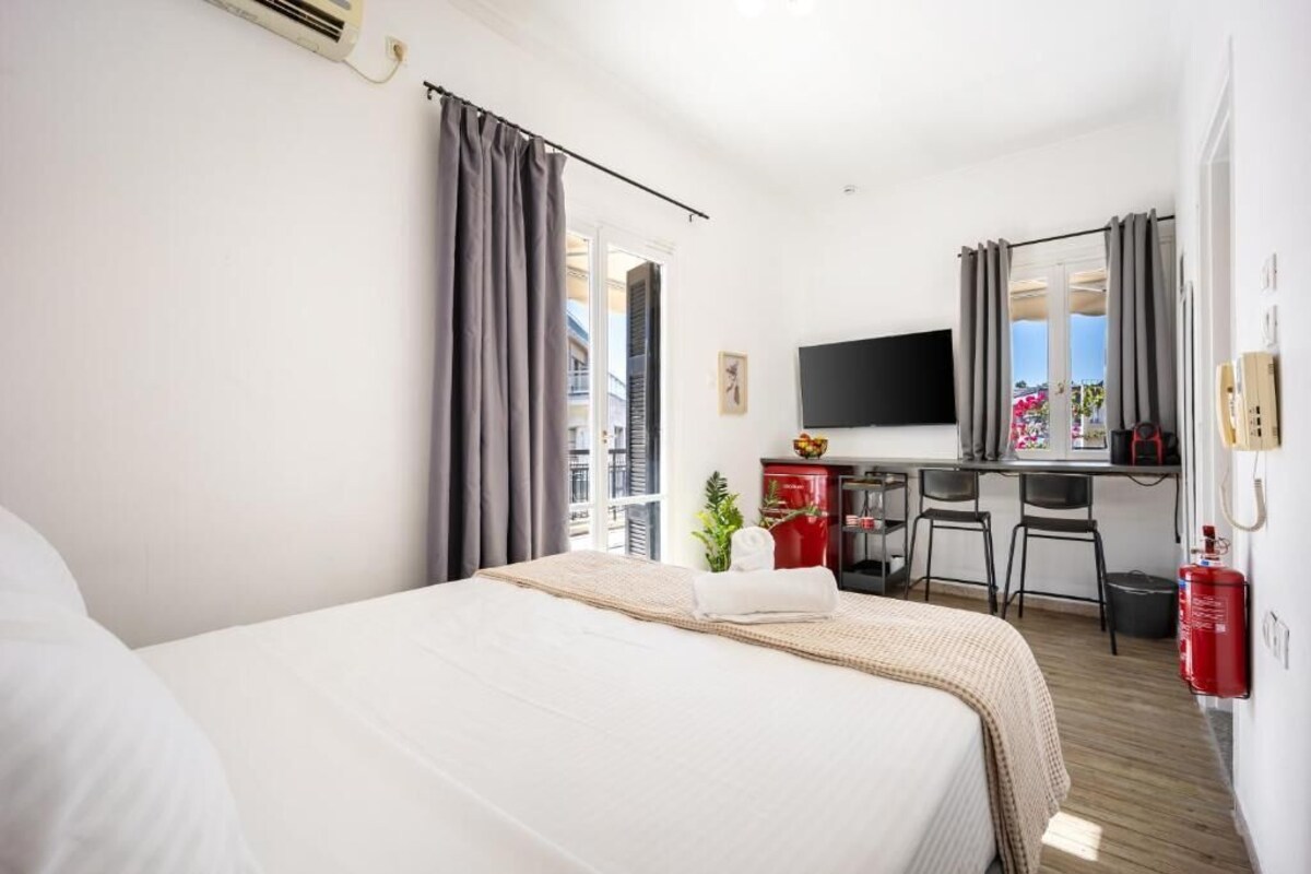 A hotel room with a bed, a desk, a chair, a television, and a fire extinguisher.