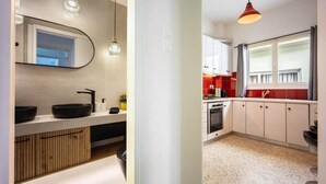 A modern kitchen with a large window, white cabinets, and a red backsplash. - Athens Nala (Athens)