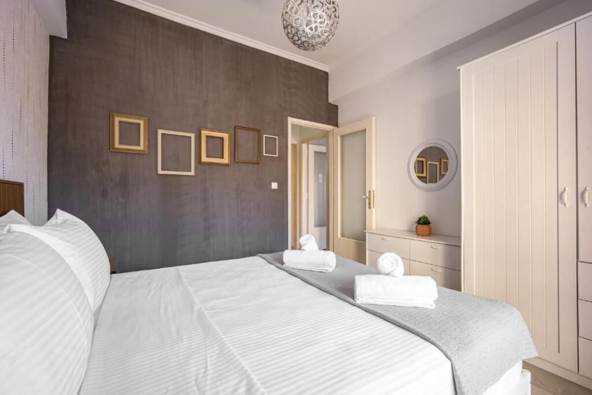 A modern bedroom with a large bed, a wardrobe, a mirror, and framed pictures on the wall.