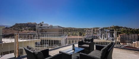 Terrassa al terrat amb mobiliari de vimet i una taula de vidre, amb vista a un paisatge urbà ple d'edificis i un turó.